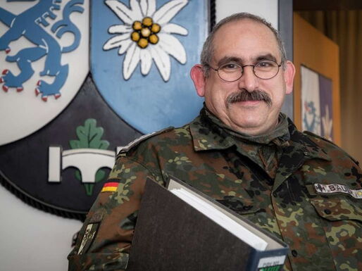 Ein Soldat mit Aktenordner unter dem Arm vor einem großen Wappen an der Wand